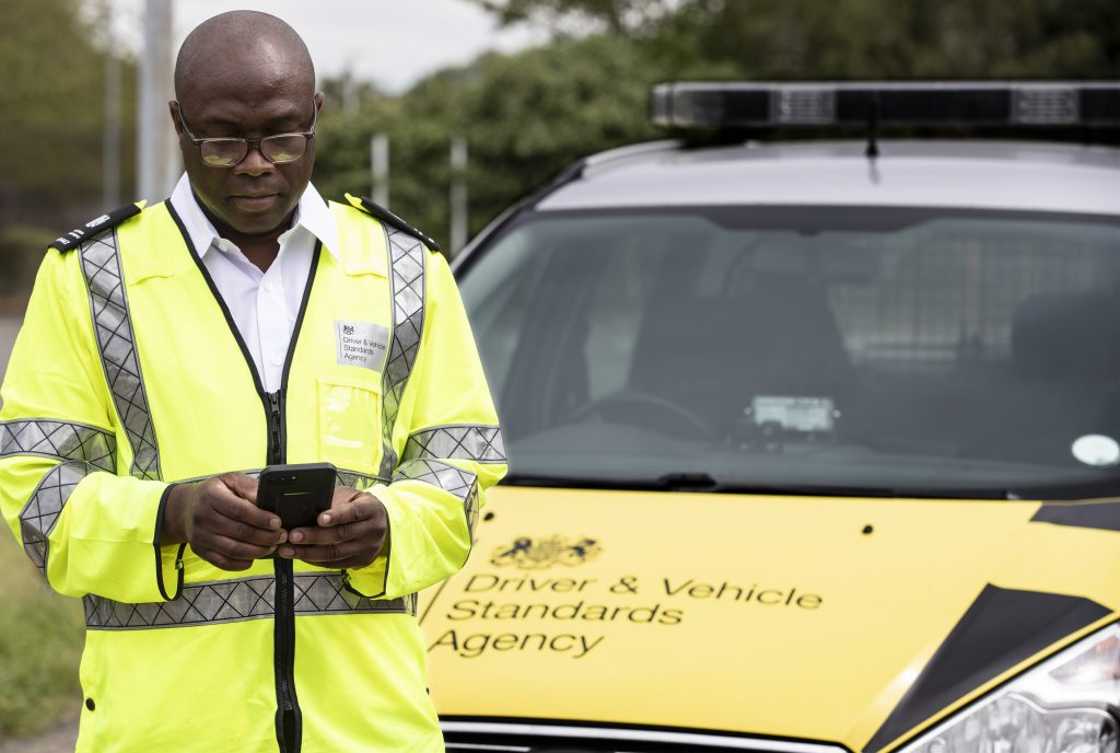 Male vehicle-examiner standing in front of a DVSA vehicle.