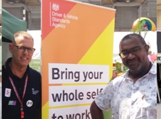 Two DVSA staff standing near a "Bring your whole self to work" DVSA sign from an event advocating equality and diversity.