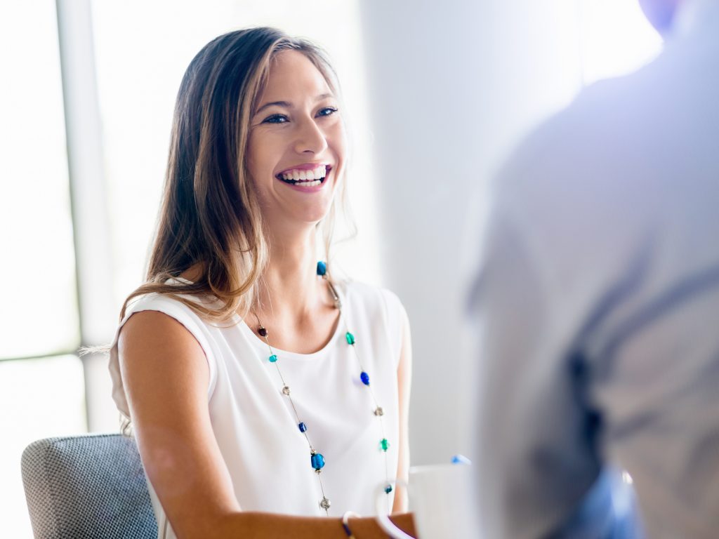 Female interviewee in white shirt, smiling as she greets a male interviewer.