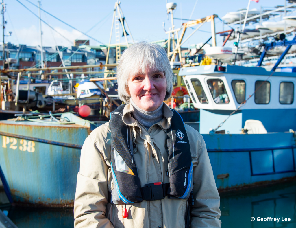 Female staff member of Maritime and Coastguard Agency, wearing a life-jacket and standing in front of a boat.