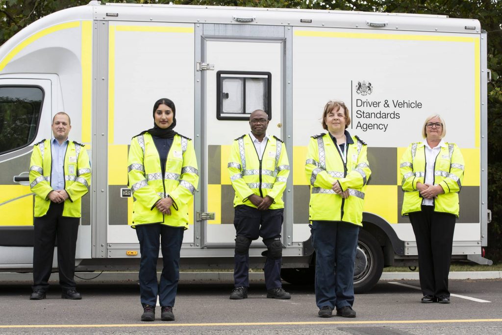 A diverse group of DVSA staff standing in front of a white DVSA van.