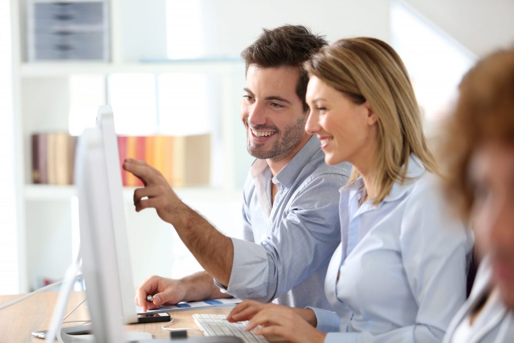 Man and woman pointing at computer screen and smiling.