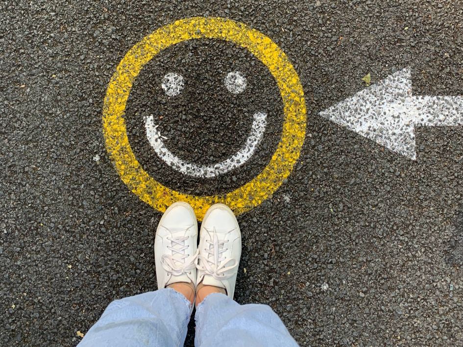 Image of a smiling face painted onto the road. Image is from a first-person angle with the photographer looking down at the smiling painting.