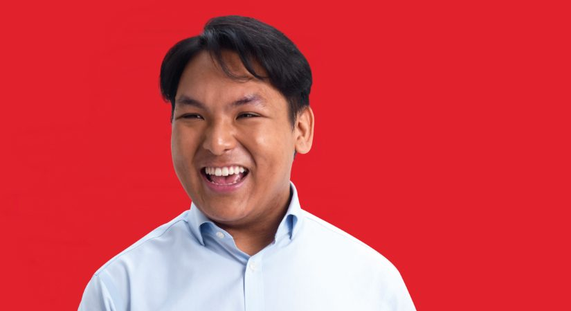 Young man smiling against red backdrop.